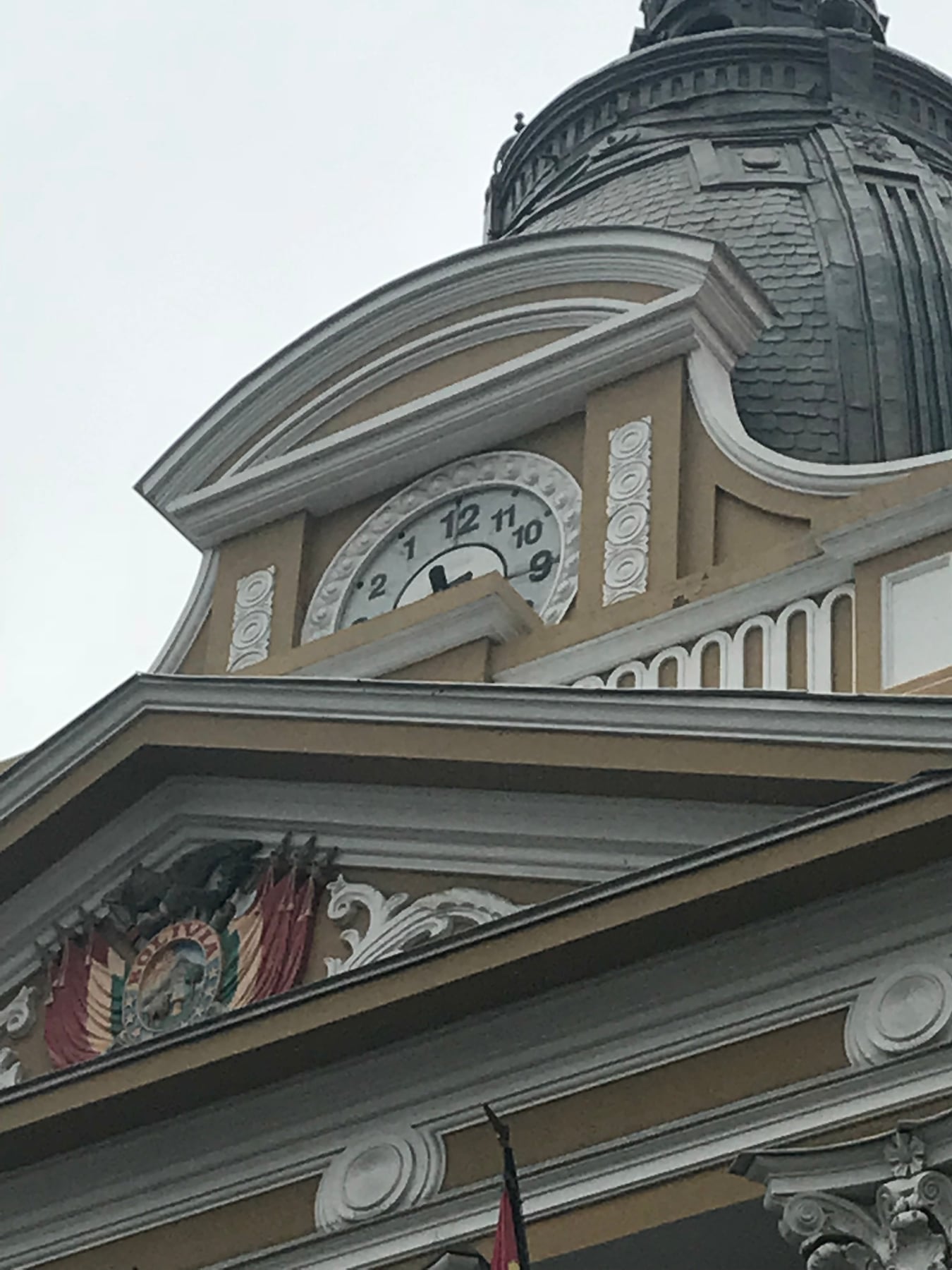 The clock on Bolivia’s Legislative Palace photographed from below, with numerals running counterclockwise: 1 and 2 to the left of 12, and 11, 10 and 9 to its right.